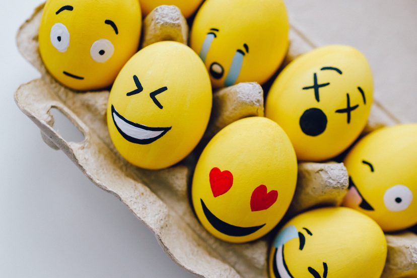A carton filled with whimsically painted emoji eggs, each one adorned in vibrant yellow hues, radiating cheerfulness and playfulness.