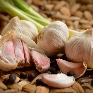 "Close-up of garlic cloves and black peppercorns on a rustic wooden surface with celery stalks in the background."