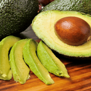 "Fresh avocados and slices on a wooden board, potentially harmful if ingested by chickens."