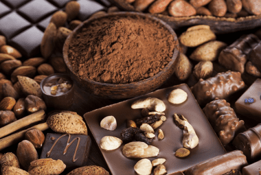 An assortment of chocolates and nuts, including cocoa powder, almonds, and various chocolate confections, unsafe for chicken consumption.
