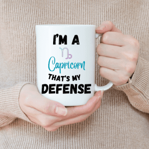 The image shows a person holding a white mug with a printed text that says, "I'M A Capricorn THAT'S MY DEFENSE" along with the symbol for Capricorn. The text uses different colors and fonts to emphasize the words and add a playful touch to the design. It appears to be a personal item, likely a novelty or a horoscope-themed mug, that reflects a sense of humor or pride in one's astrological sign.