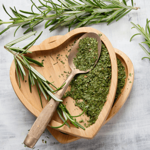 Fresh rosemary sprigs and dried rosemary leaves on wooden heart-shaped trays with a rustic spoon.