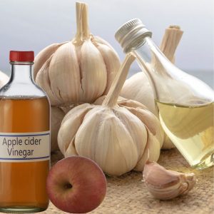 Garlic bulbs, a bottle of apple cider vinegar, and an apple on a wooden surface.
