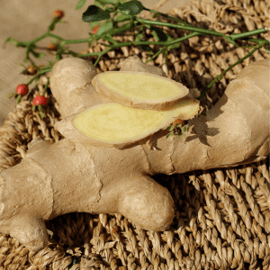  Close-up of fresh ginger root with a few slices on a woven mat, accompanied by small red berries and green stems.